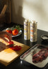 Both Argo tins on a kitchen counter with tomato, bread and garlic